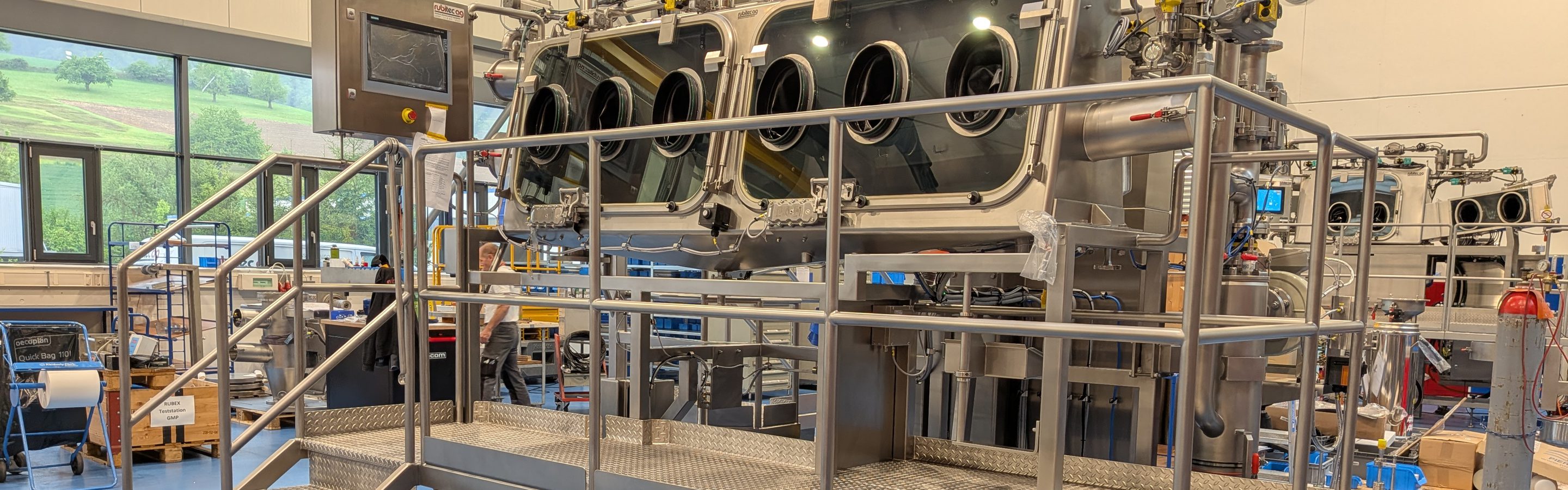 Containment-Isolator von rubitec ag mit Handschuheingriffen auf fahrbarer Bedienbühne in der Fertigung in Bennwil